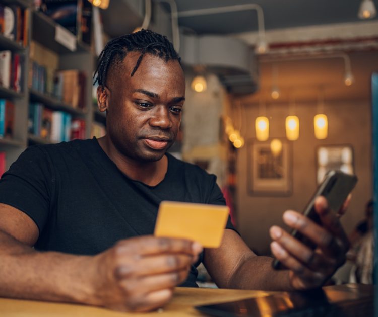 African american man using smartphone and credit card in a cafe