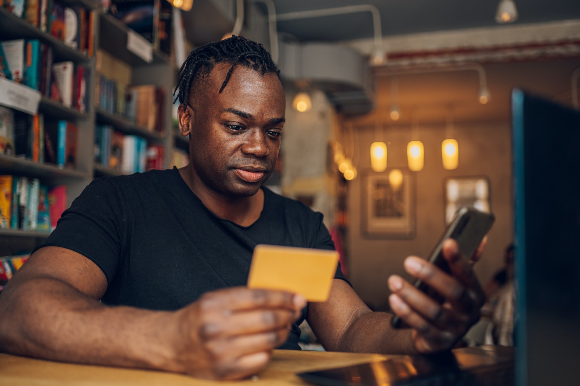 African american man using smartphone and credit card in a cafe